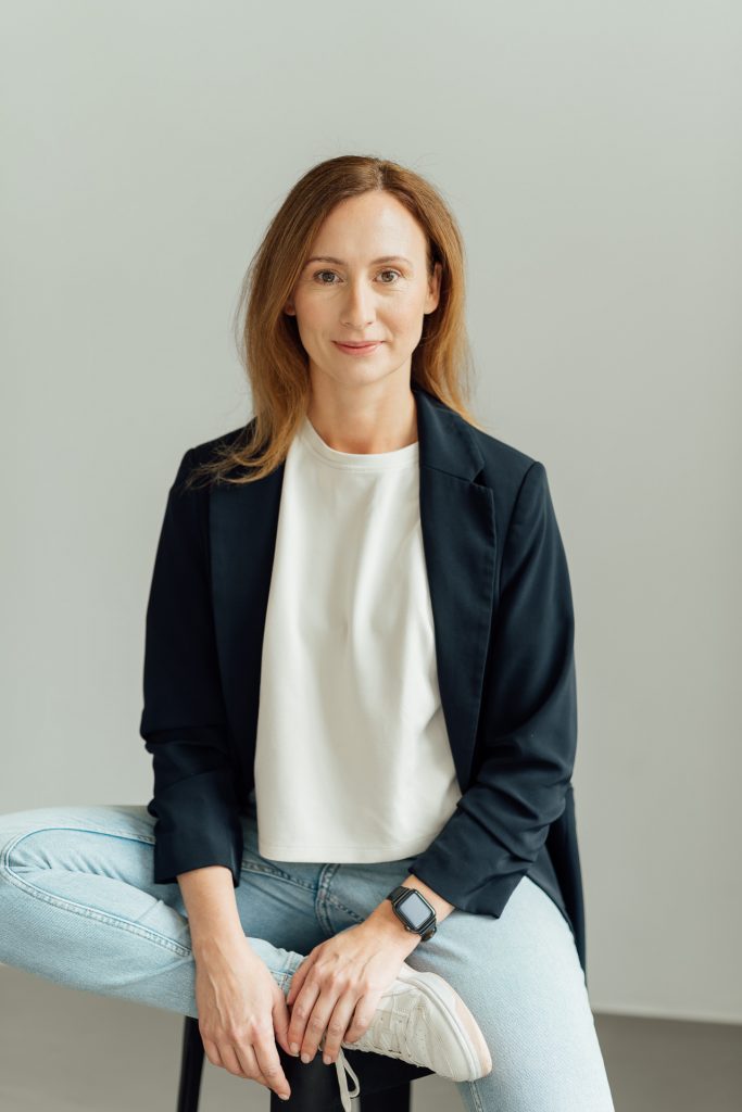 Diana Bluhm sitzt auf einem Hocker und schaut in die Kamera